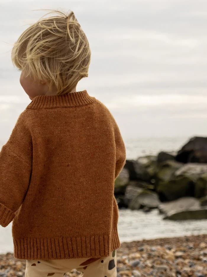 A child on a pebble beach in an Organic Zoo knitted jumper